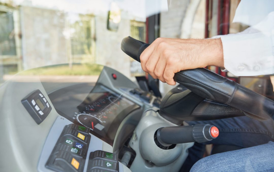 Unrecognizable man wearing shirt driving intercity bus at daytime. Crop view of male professional bus driver steering wheel at work. Concept of transportation, work place.